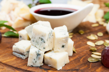 Several types of cheese on a wooden plate with berry sauce.