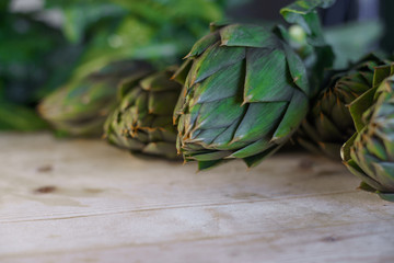 Fototapeta premium Close up of thorns leaves of the artichokes freshly picked by the farmer laid on a wooden table and illuminated by sunlight, vegan and mediterranean cuisine ingredients