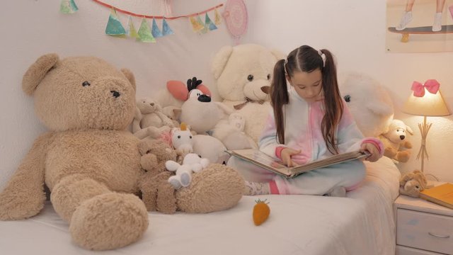 ni&ntilde;a con pijama con coletas rodeada de mu&ntilde;ecos de peluche ojea un &aacute;lbum de fotos