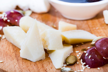Several types of cheese on a wooden plate with berry sauce.
