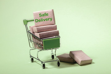 Stack of packed boxes in mini shopping trolley with label Safe Delivery and on floor. Light green...