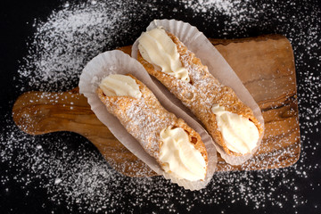 Top view of two delicious cannoli on black background