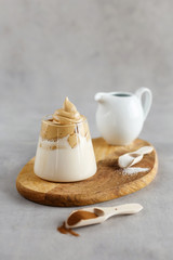 Korean drink. Homemade dalgona coffee in glass with milk on grey background. Trendy fluffy creamy whipped coffee.  Wooden stand.