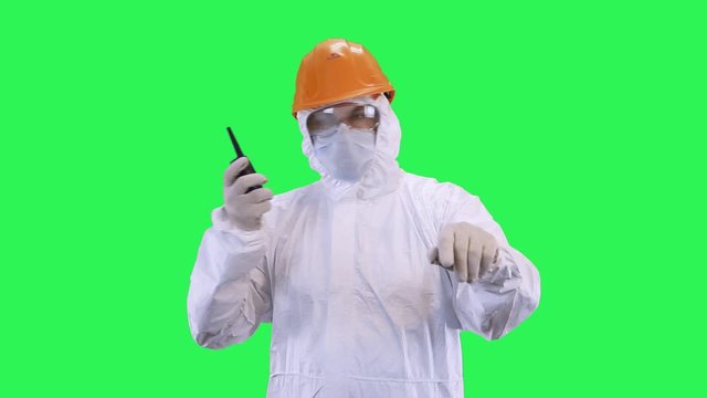 A man in a helmet and protective suit speaks on the radio in elevated tones.Green screen background.