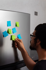 Hispanic young man taking and reading sticky posticks in his fridge