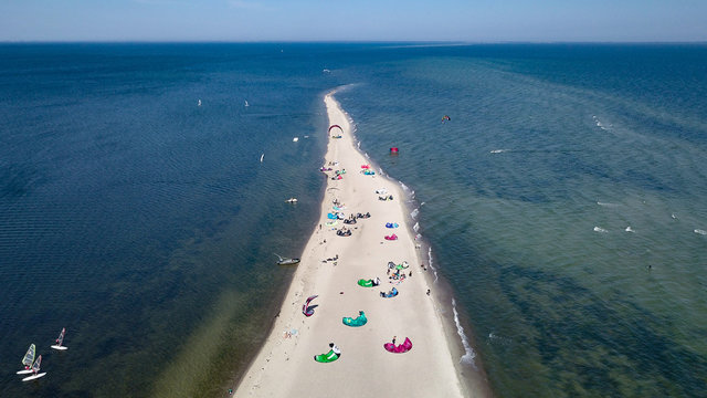 Aerial view of white sand beach peninsula with kites for kite surfing laying down on the beach and some kite surfers flying on the waves. Polish seaside coast with Baltic Sea's waters.