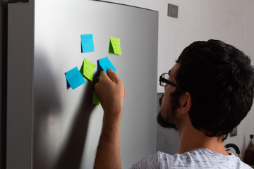 Hispanic young man taking and reading sticky posticks in his fridge