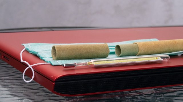 A Greenish Gauze Bandage, A Medical Thermometer And A Cardboard Pencil Case From It On A Laptop Cover