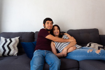 Obraz premium Young adult Hispanic married couple.hugging on the couch and smiling as they rest on a couch