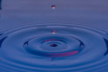 Gotas de agua color azul con morado suspendidas en el aire y  formando ondas en la superficie...