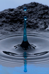 Gotas de agua color azul congeladas en el aire y formando ondas en la superficie liquida, con rocas...