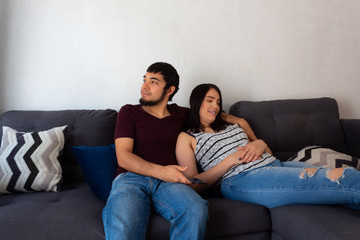 Young adult Hispanic married couple.hugging on the couch and smiling as they rest on a couch