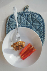 Still life of food with white plate and fork on blue kitchen towel. A piece of meat and red paprika on the plate.