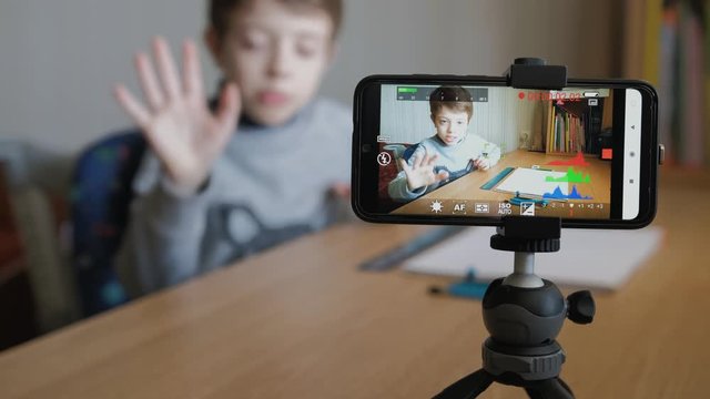 Schoolboy makes his first video blog. He draws a car with a pencil, ruler and drawing compass. Using his phone and mini tripod to shoot video.