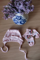 Beautiful pink baby clothes. Home cosiness. baby booties and clothes with a bouquet of flowers on the background. Newborn clothes