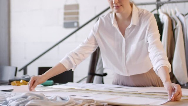 Professional female dressmaker laying out paper pattern on fabric and pinning it while working in sewing studio
