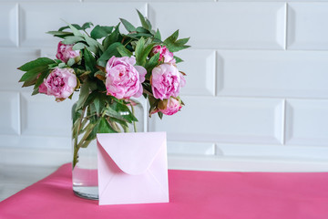 Bouquet of pink peonies in glass vase against white background and wooden table. Mothers day card. Beautiful peony flower for catalog or online store. Floral shop and delivery concept. Copy space.