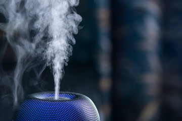 Aromatherapy oil diffuser with blue LED light from which steam comes out on a dark background....
