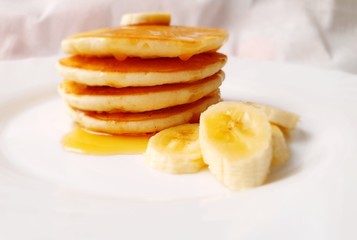 PLATO DE PANCAKES (TORTITAS) CON MIEL Y PLÁTANO EN FONDO BLANCO.