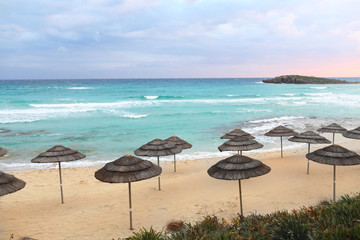 Straw umbrellas on a beach with sea blue sky with sunset. Nobody. Clear horizon. selective focus. copy space