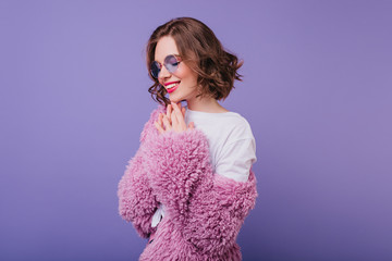 Fashionable woman with wavy hairstyle smiling with eyes closed. Indoor photo of enthusiastic female...