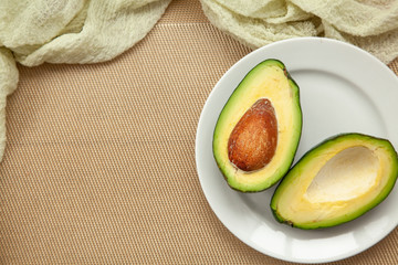 Two halves of ripe avocado on white plate and a wooden background.