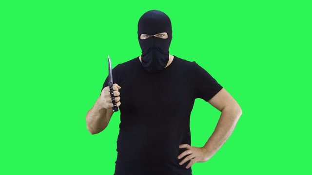A man in a black mask holds a knife in his hand.Balaclava.Green screen background.