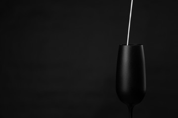 Matte black glass on a black background. Dark mode. Copy space. Minimalism. White stream of milk