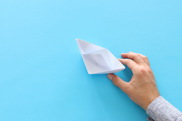 male hand directing single papaer boat on blue background. concept of finding the right directon and moving ahead.