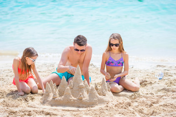 Father and kids making sand castle at tropical beach. Family playing with beach toys