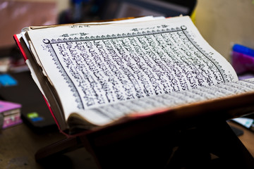 Quran, the Scripture of Muslims on rihal or wood book stand, prayer beads or tasbeeh, skullcap hat, at home.  The concept of staying home in ramadan during a corona virus disease pandemic situation.