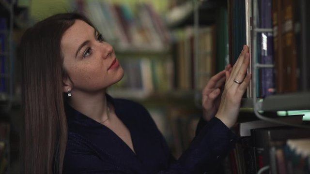 Beautiful Girl along beetwen the shelves in the library looking for specific book