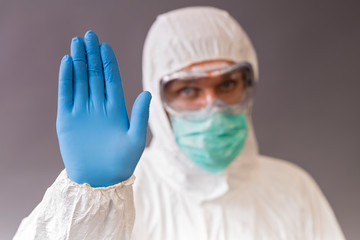 Male doctor with surgical mask, goggles and protective suit showing stop on gray backround.