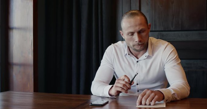 Stressed office worker in white shirt making call after consideration and waiting a while then hanging up and murmuring angrily while sitting at table.