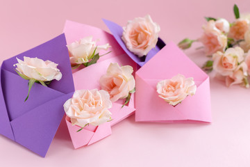 Purple and pink paper open envelopes with full small rose flowers on color background. Spring, summer concept. Romance, love notes, greeting card for March 8 International Woman's, Valentine's day