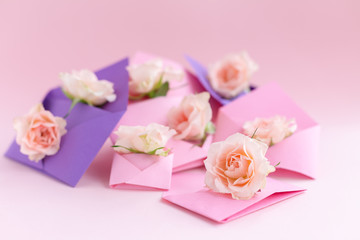 Purple and pink paper open envelopes with full small rose flowers on color background. Spring, summer concept. Romance, love notes, greeting card for March 8 International Woman's, Valentine's day