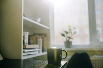 Cup with coffee on table near shelves on window background