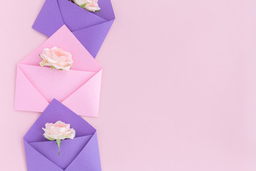 Purple and pink paper open envelopes with full small rose flowers on color background. Spring, summer concept. Romance, love notes, greeting card for March 8 International Woman's, Valentine's day