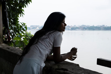 Portrait of a beautiful dark skinned brunette Indian lady in white ethnic dress standing in front of a lake in a sunny morning. Indian lifestyle.