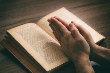 Naklejka premium Hands clasped in prayer over a Holy Bible, wooden table background.