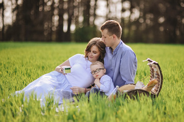 Family on a picnic in the forest. In the meadow. Picnic basket with food. The dog runs and wants to play. A child with glasses. Blue color in clothes. To eat outdoors. Time with family.