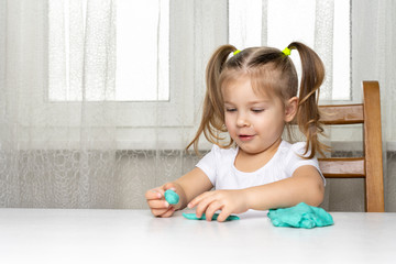girl preschooler sits at a table and sculpts from turquoise dough for modeling. activities with children at home on self-isolation in connection with coronavirus infection