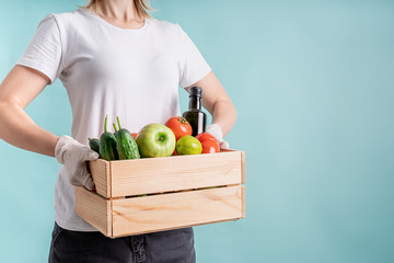 Blond woman in gloves holding a wooden box full of vegetables with copy space
