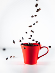 
Roasted coffee beans, dipping into a red coffee cup, on a white background