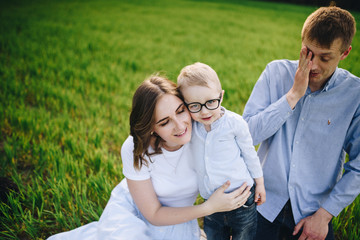 Obraz premium Family on a picnic in the forest. In the meadow. Picnic basket with food. The dog runs and wants to play. A child with glasses. Blue color in clothes. To eat outdoors. Time with family.