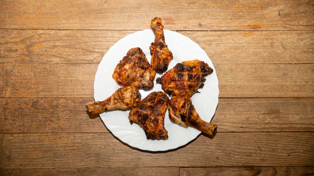 Chicken legs marinated in spices, grilled, arranged in a white plate, on a woody background