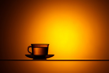 Cup and saucer with a transparent liquid on a bright orange background. Water or tea in the light.