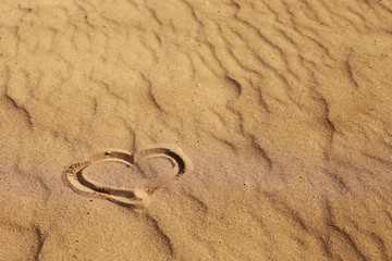 Fototapeta na wymiar Heart drawn on the sand, concept of love. Relax on the sandy beach. Copy space. Valentine's day on a sunny beach.