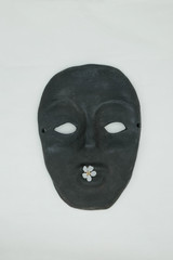  Black ceramic mask on a white background. White flower on lips mask. Mass produced mask. Copy space.