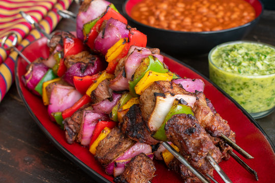 Steak Fajita Skewers with Cilantro Chimichurri: Grilled beef and vegetable kabobs served with chimichurri sauce and pinto beans